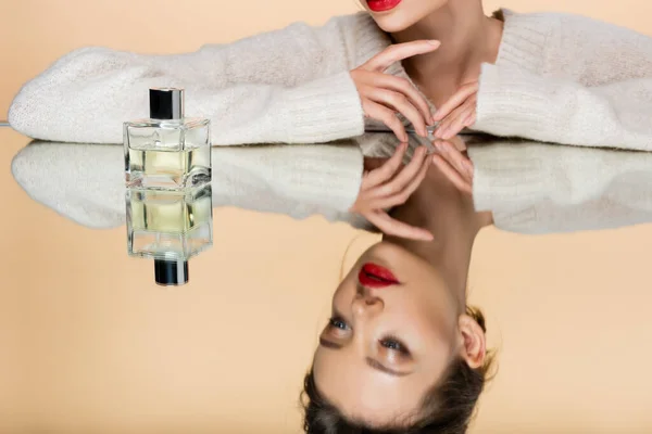 Ausgeschnittene Ansicht einer Frau im Pullover in der Nähe von Parfüm auf Spiegel isoliert auf beige — Stockfoto