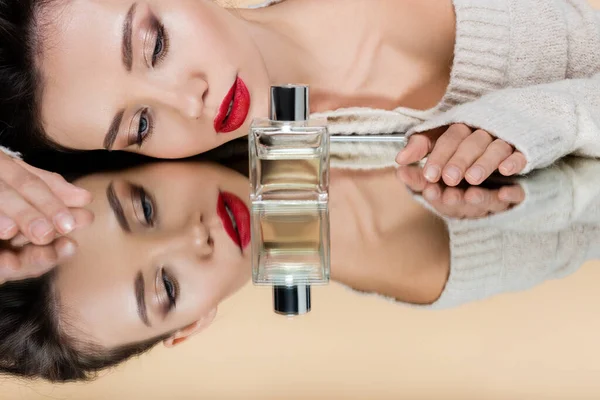Stylish woman with red lips lying near perfume bottle on mirror on beige background — Stock Photo