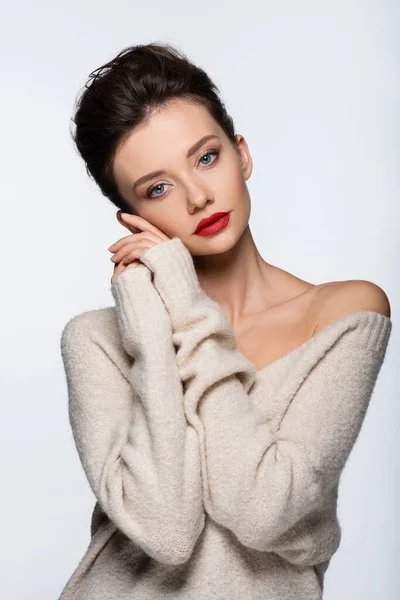 Молодая модель в свитере с обнаженным плечом, смотрящая на камеру, изолированную на белом — стоковое фото