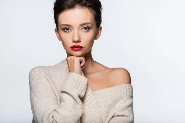 Pretty model in sweater with naked shoulder holding hand near chin isolated on white — Stock Photo