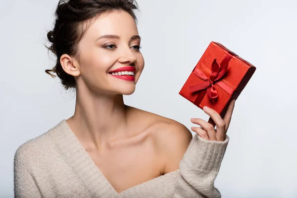Stylish model in sweater with naked shoulder holding present and smiling isolated on white — Stock Photo