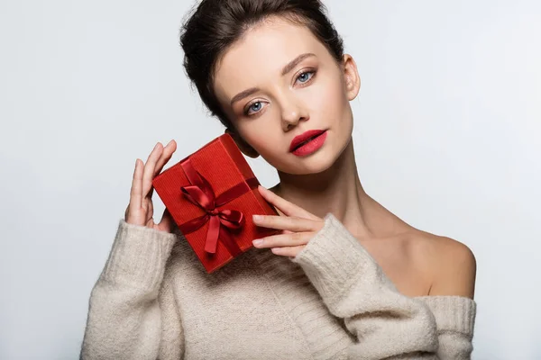 Modelo morena en suéter posando con regalo rojo aislado en blanco - foto de stock