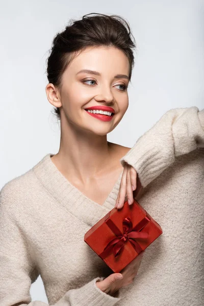 Mujer feliz en suéter acogedor sosteniendo caja de regalo roja aislada en blanco - foto de stock