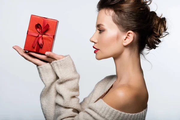 Vue latérale de la femme brune élégante regardant le présent rouge isolé sur blanc — Photo de stock