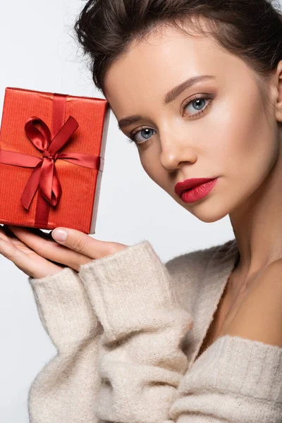 Portrait of young model in sweater holding present and looking at camera isolated on white — Stock Photo