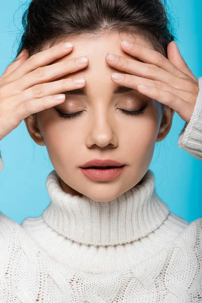 Portrait of young brunette woman in sweater touching forehead isolated on blue — Stock Photo