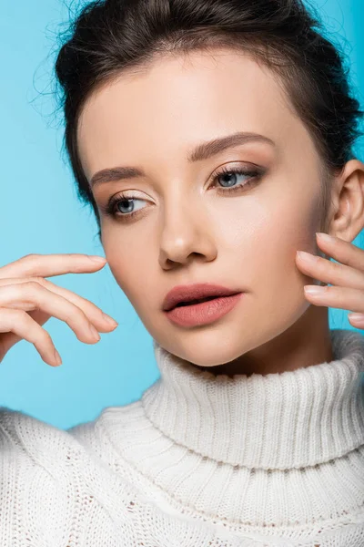 Jolie jeune femme en pull blanc touchant visage isolé sur bleu — Photo de stock