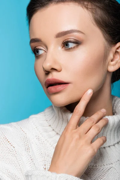 Young model in sweater touching cheek isolated on blue — Stock Photo