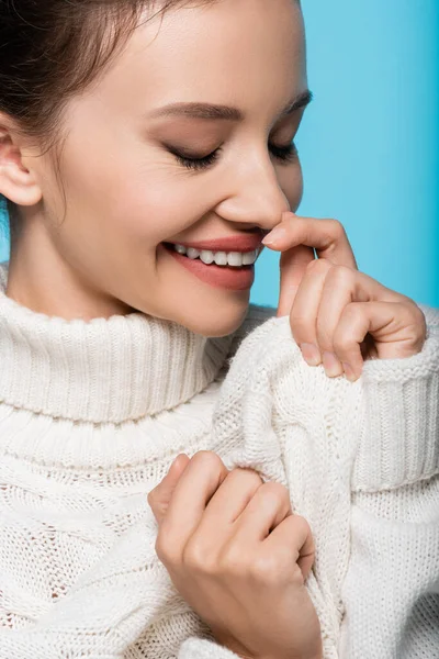 Retrato de mujer sonriente en suéter acogedor cerrando los ojos aislados en azul - foto de stock