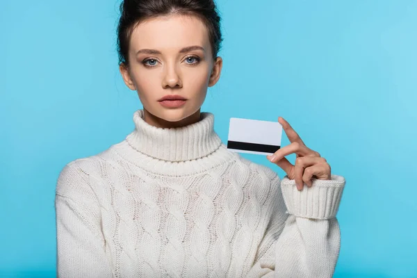 Junge Frau im Strickpullover hält Kreditkarte isoliert auf blauem Grund — Stockfoto