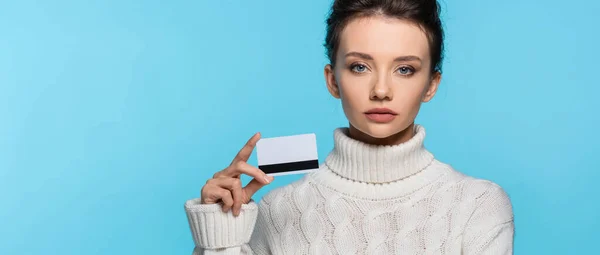 Молода жінка в теплому светрі тримає кредитну картку ізольовано на синьому, банер — стокове фото