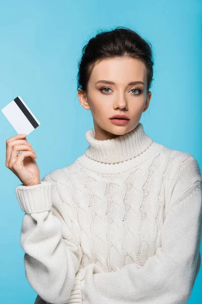 Joli modèle en pull tricoté tenant la carte de crédit isolée sur bleu — Photo de stock