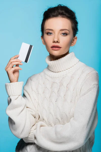 Jolie jeune femme en pull chaud tenant la carte de crédit isolée sur bleu — Photo de stock