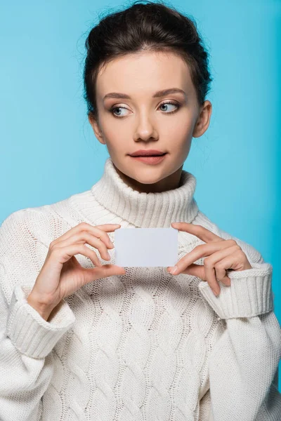 Pensive woman in sweater holding blank card isolated on blue — Stock Photo