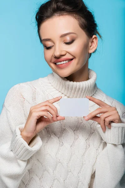 Lächelndes Model in weißem Pullover mit leerer Karte auf blauem Hintergrund — Stockfoto