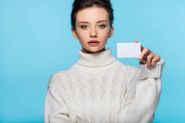 Jovem mulher de malha suéter segurando cartão em branco e olhando para a câmera isolada no azul — Fotografia de Stock