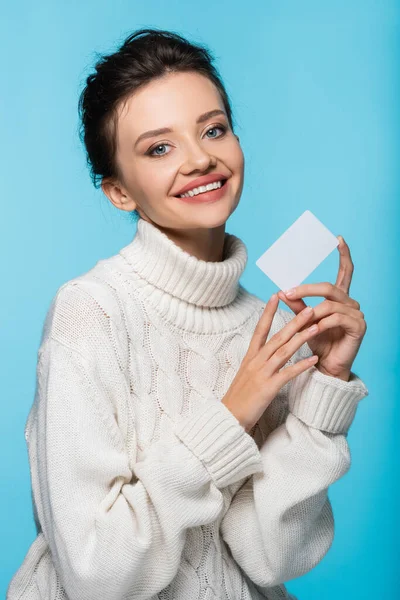 Fröhliche Frau in weißem Strickpullover mit leerer Karte auf blauem Hintergrund — Stockfoto