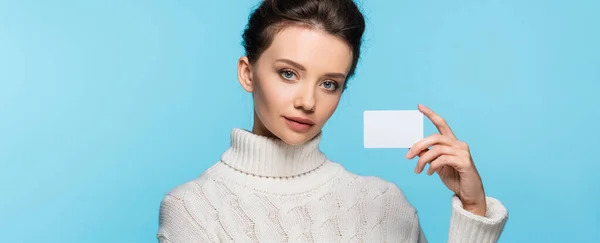 Modelo morena en suéter de punto que sostiene la tarjeta en blanco aislado en azul, bandera — Stock Photo