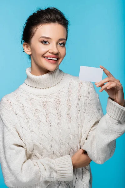 Positive woman in white sweater holding blank card with copy space isolated on blue — Stock Photo