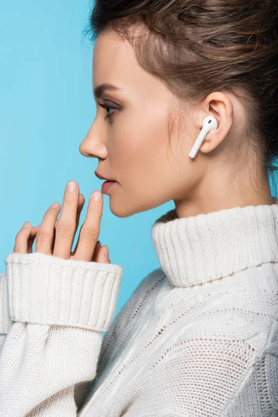 Vue latérale de la femme brune en écouteur sans fil et pull isolé sur bleu — Photo de stock