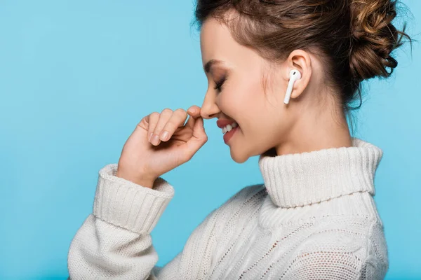 Side view of cheerful woman in knitted sweater and earphone isolated on blue — Stock Photo