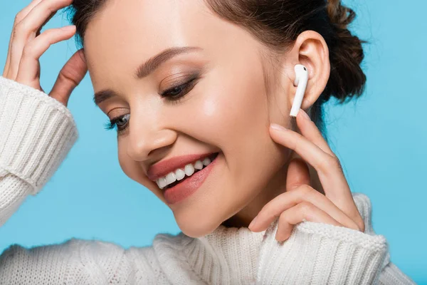 Portrait of smiling model in knitted sweater using earphone isolated on blue — Stock Photo