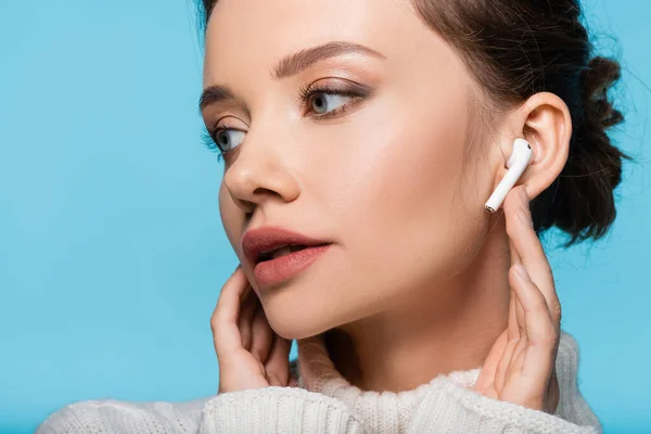 Young model in sweater using wireless earphone isolated on blue — Stock Photo