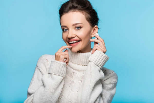 Happy brunette woman in sweater holding earphone isolated on blue — Stock Photo