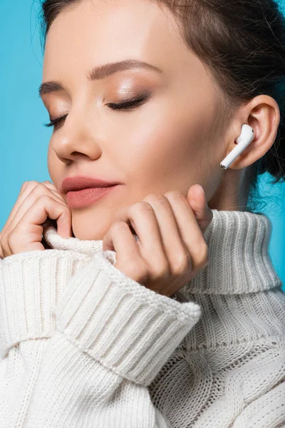 Portrait of woman with closed eyes wearing sweater and using earphone isolated on blue — Stock Photo
