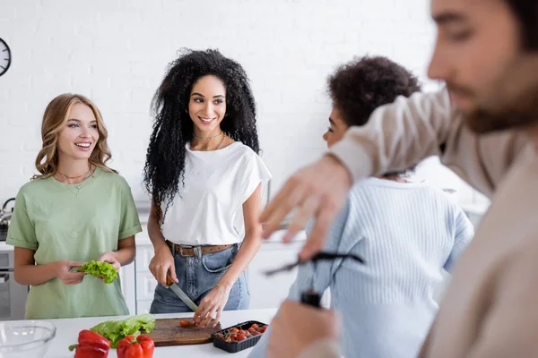 Happy multiethnic woman looking at each other while blurred man opening bottle of wine — Stock Photo