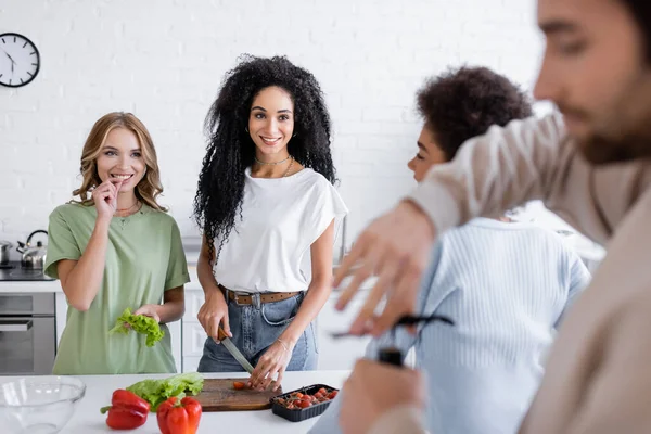 Happy multiethnic woman looking at blurred man opening bottle of wine — Stock Photo