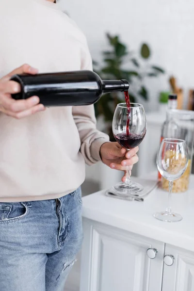 Abgeschnittene Ansicht eines Mannes, der in der modernen Küche Rotwein ins Glas gießt — Stockfoto