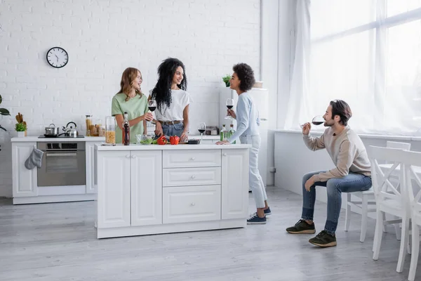 Happy lesbian couple cooking near interracial friends with glasses of wine — Stock Photo