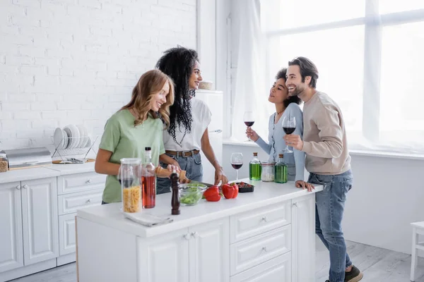 Cheerful lesbian couple cooking near interracial friends with glasses of wine — Stock Photo