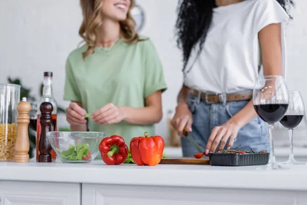 Cropped view of lesbian couple cooking near glasses of red wine in kitchen — Stock Photo