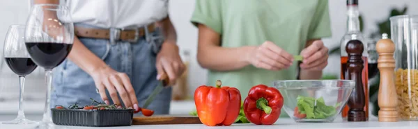 Vista ritagliata di coppia lesbica cottura insalata vicino a bicchieri di vino rosso in cucina, banner — Foto stock