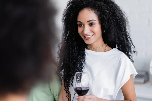 Happy african american woman holding glass of wine in kitchen — Stock Photo