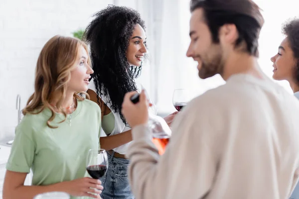 Feliz interracial mulher ter conversa perto borrado satisfeito homem segurando garrafa — Fotografia de Stock