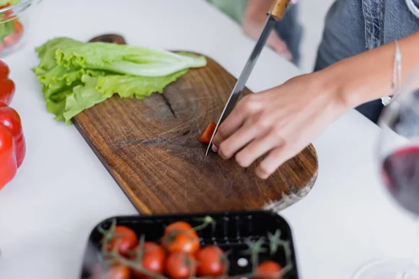 Cropped view of woman cutting cherry tomato on chopping board — Stock Photo