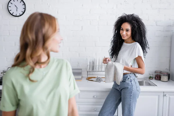 Encaracolado Africano americano mulher olhando para namorada loira na cozinha — Fotografia de Stock
