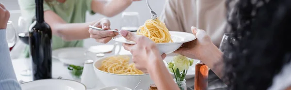 Cropped view of woman serving pasta to blurred friend, banner — Stock Photo