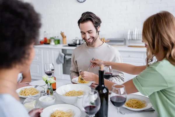 Donna bionda che serve la pasta all'uomo allegro vicino a un amico afroamericano offuscato — Foto stock