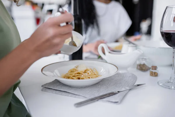 Abgeschnittene Ansicht einer Frau, die eine Schüssel mit geriebenem Käse in der Nähe von Pasta auf einem Teller hält — Stockfoto