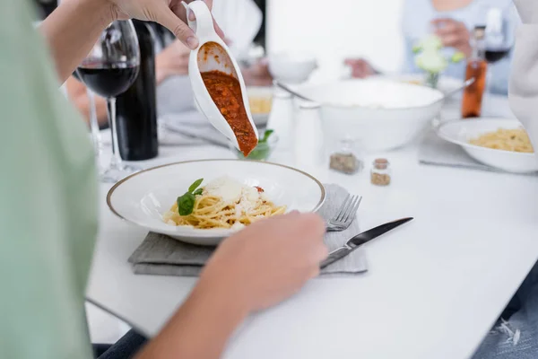 Abgeschnittene Ansicht einer Frau, die Bolognese-Sauce in Pasta mit geriebenem Käse auf Teller gießt — Stockfoto