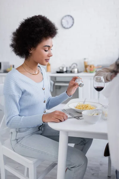 Young african american woman salting pasta near glass of red wine — Stock Photo