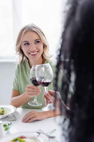 Feliz pareja lesbiana tintineo vasos de vino tinto durante el almuerzo - foto de stock