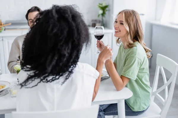 Feliz pareja lesbiana cogida de la mano durante el almuerzo con amigo - foto de stock