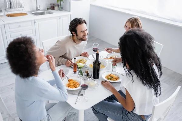 Vista de ángulo alto del hombre feliz riendo cerca de amigos multiétnicos durante el almuerzo - foto de stock