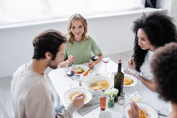 Cheerful multiethnic women looking at friend near pasta on plates — Stock Photo
