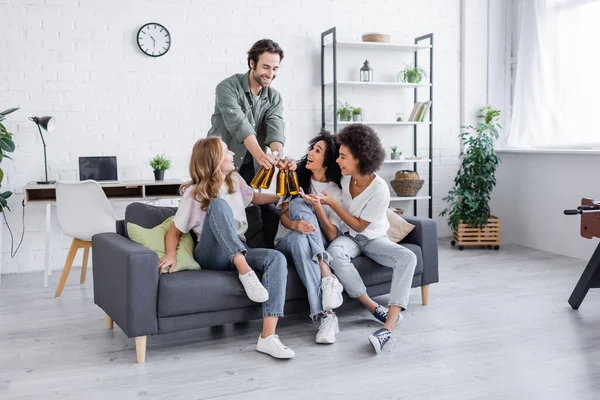 Glücklicher Mann mit Bierflaschen neben fröhlichen interrassischen Freunden auf dem Sofa — Stockfoto